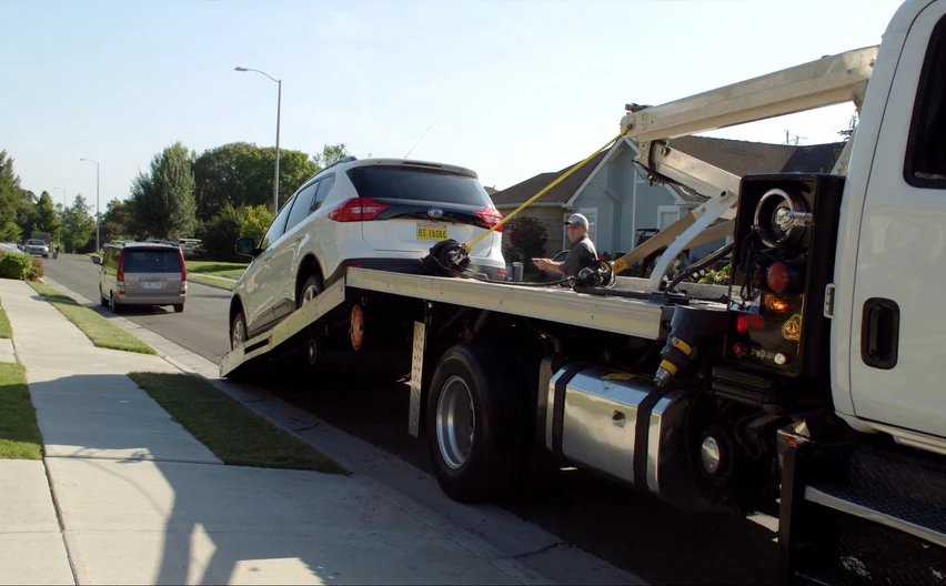 A flatbed tow truck loading a sedan on the shoulder of a highway