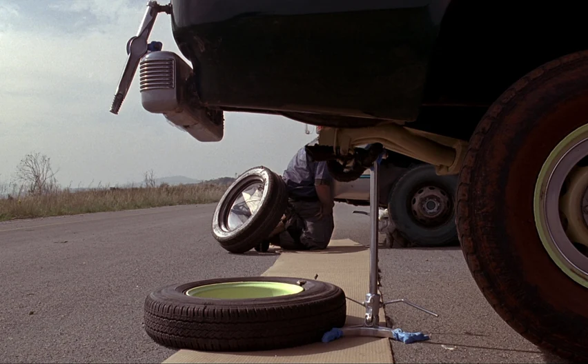 A spare wheel being fitted at the roadside with a jack under the sill